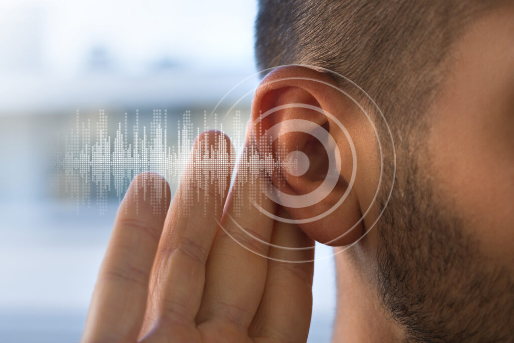 Close-up of a man cupping his hand to his ear with a digital sound wave graphic overlay, representing hearing health and sound detection.